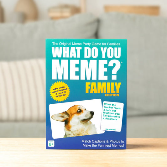 Board game box for 'What Do You Meme?' Family Edition on a table with a blurred background